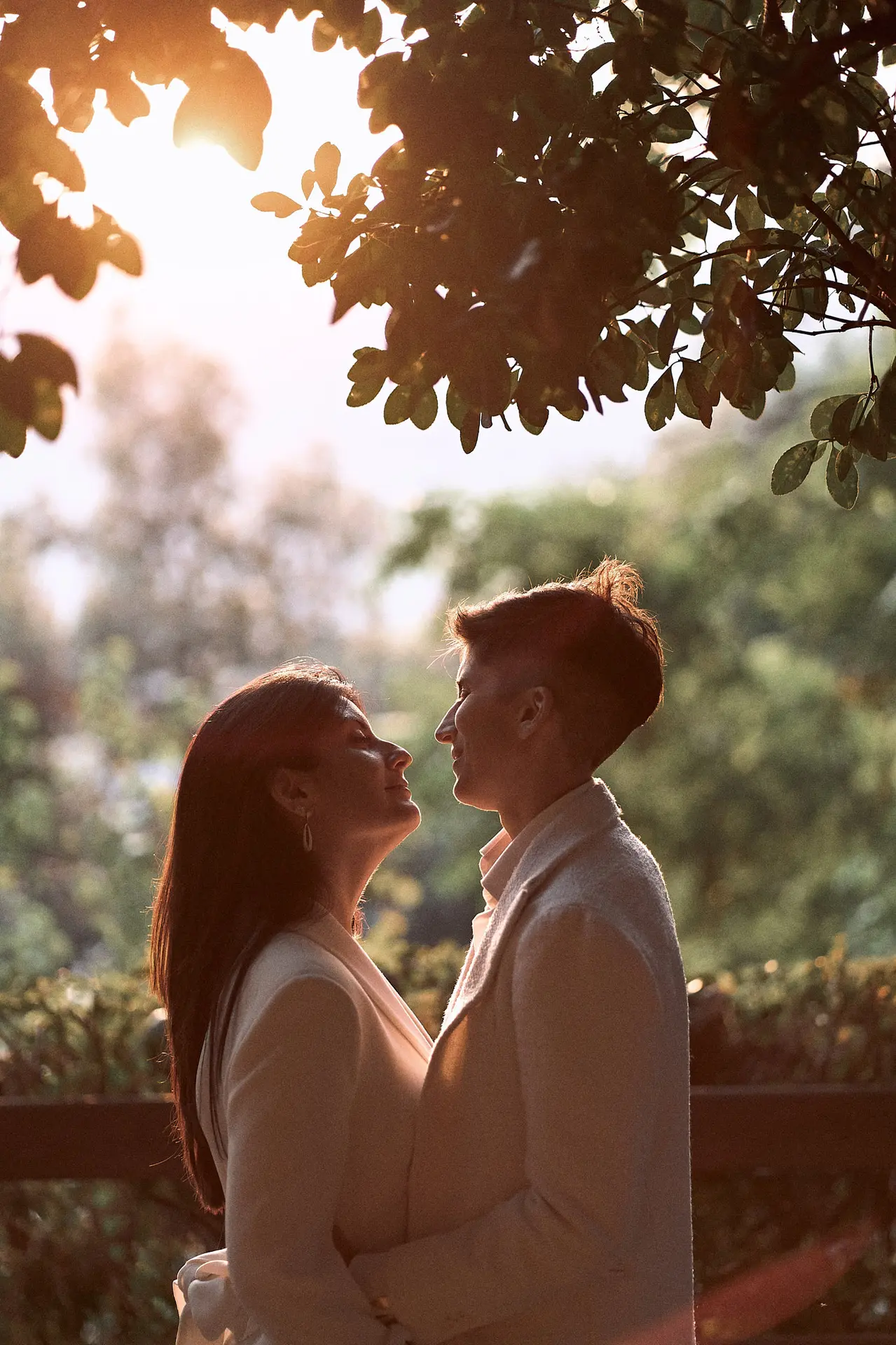 Intimate silhouette of a couple facing each other under sunlit trees.