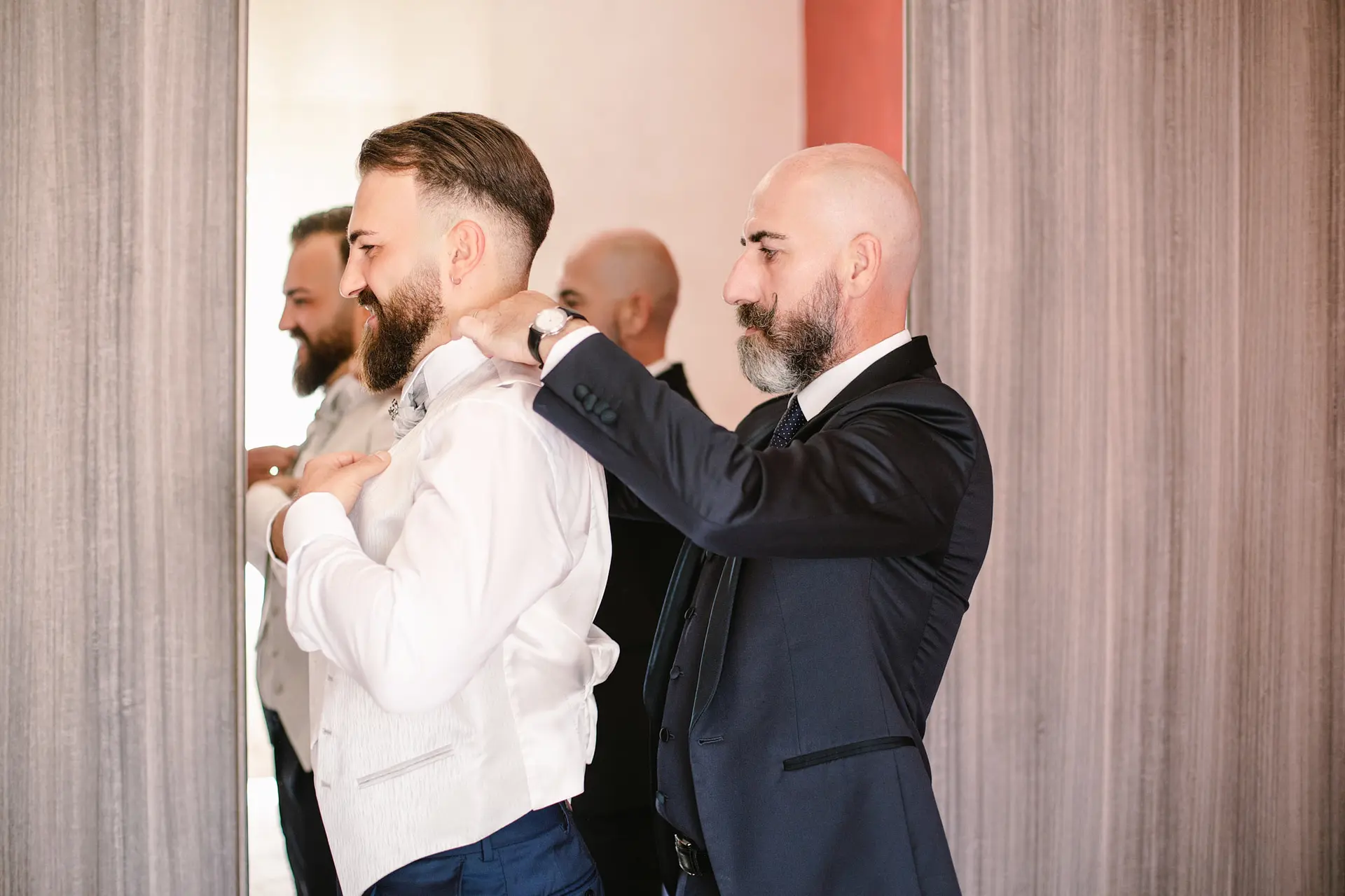 Groom smiles as his best man helps him adjust his suit jacket, getting ready for the big day.