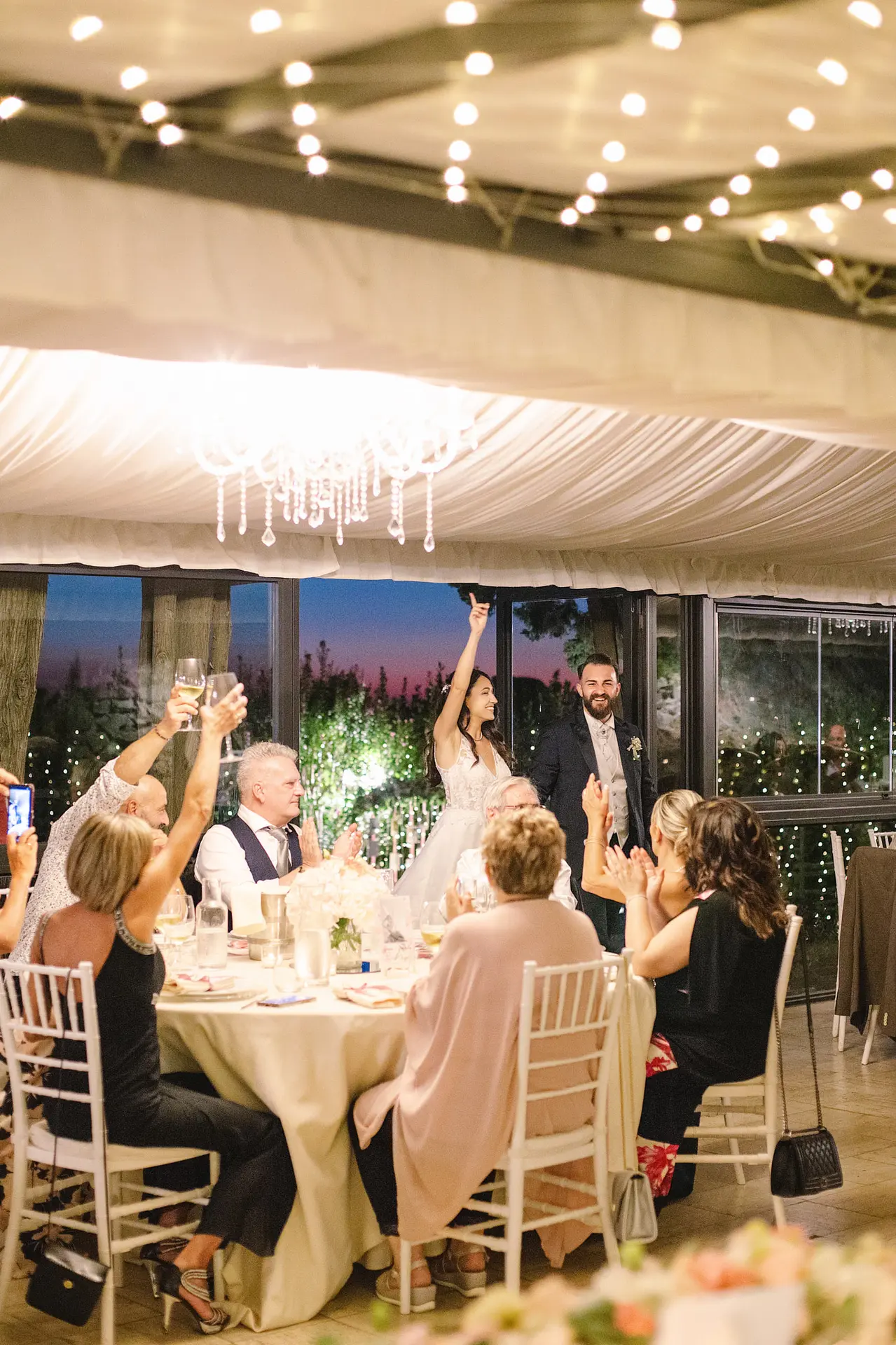 Joyful bride and groom cheered by guests as they enter their lively wedding reception under string lights.