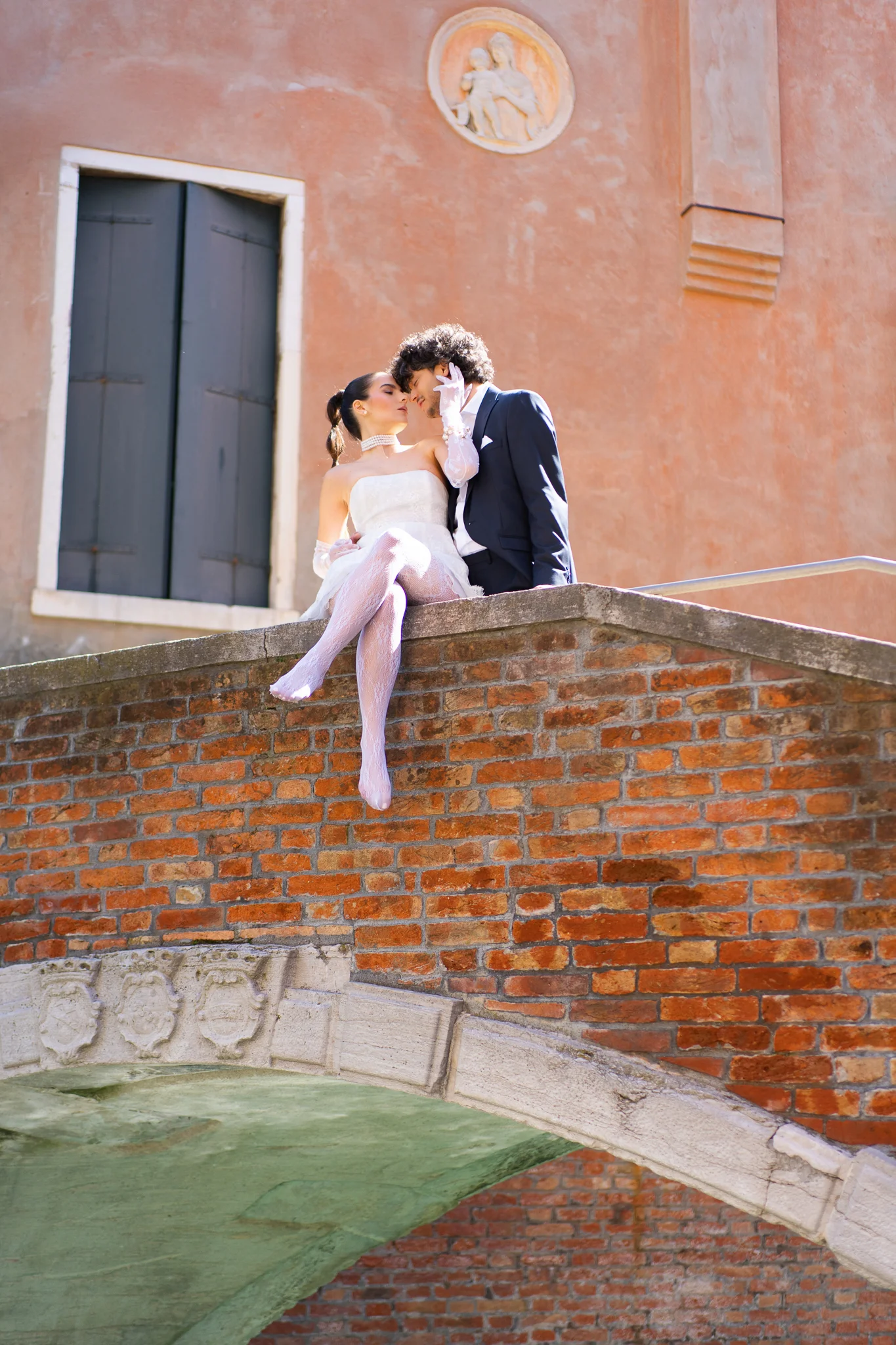 A couple shares a kiss while sitting on a charming brick bridge in Venice, showing how to elope in Italy.