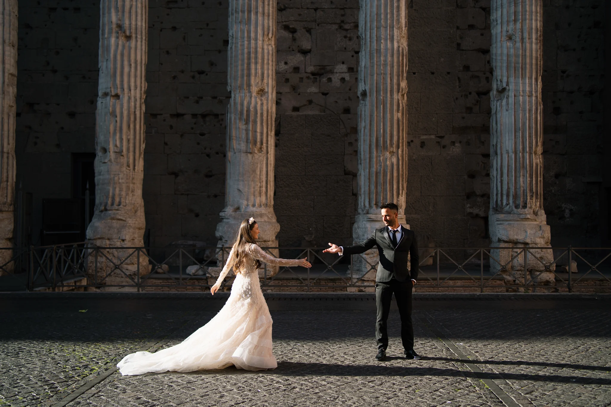 A groom reaches for his bride in front of ancient Roman columns, an epic idea for how to elope in Italy.